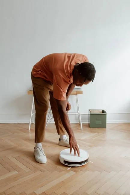 Two women in work clothes cleaning a modern living room using a vacuum and mop.